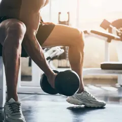 Mężczyzna wykonuje trening ekscentryczny bicepsów z hantlem, siedząc na ławce w siłowni.