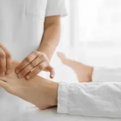 Fizjoterapeuta masuje stopę pacjenta, co może pomóc w leczeniu opadającej stopy. Warto sprawdzić, jakie witaminy przy opadającej stopie mogą wspomóc regenerację.