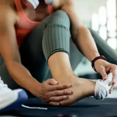 Kobieta z bólem kostki, zastanawia się czym smarować skręconą kostkę. Obok leży but sportowy.