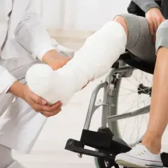 Lekarz zakłada gips na nogę po złamaniu. Pacjent siedzi na wózku inwalidzkim, czekając na powrót do zdrowia.