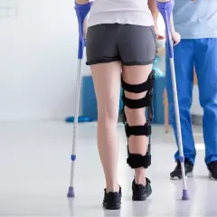 Rehabilitacja po zespoleniu gwoździem gamma. Pacjentka w ortezie na nodze, wspierając się kulami, rozpoczyna powrót do sprawności.