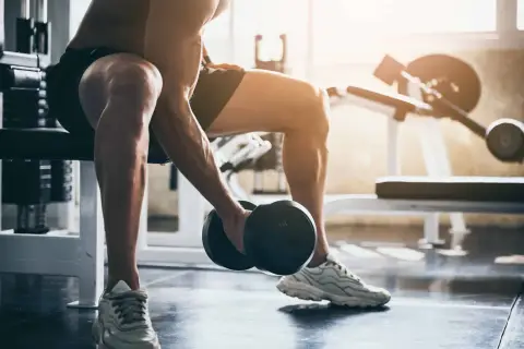 Mężczyzna wykonuje trening ekscentryczny bicepsów z hantlem, siedząc na ławce w siłowni.