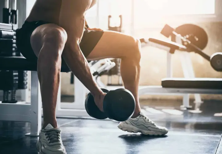 Mężczyzna wykonuje trening ekscentryczny bicepsów z hantlem, siedząc na ławce w siłowni.