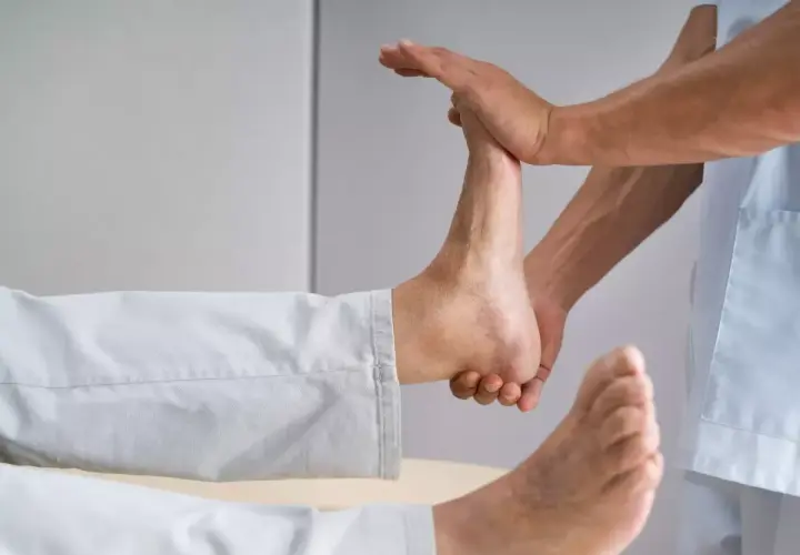 Fizjoterapeuta wykonuje ćwiczenia na opadającą stopę, delikatnie unosząc ją.