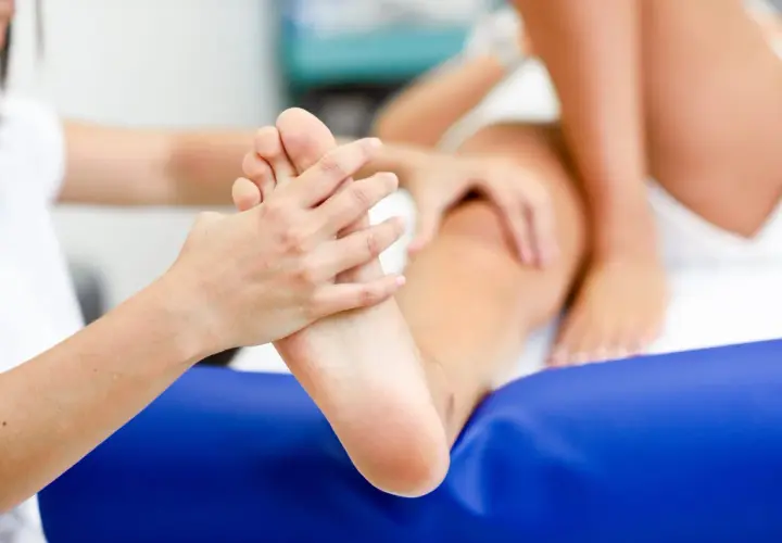 Fizjoterapeuta bada stopę pacjenta, oceniając potencjalną asymetrię chodu.