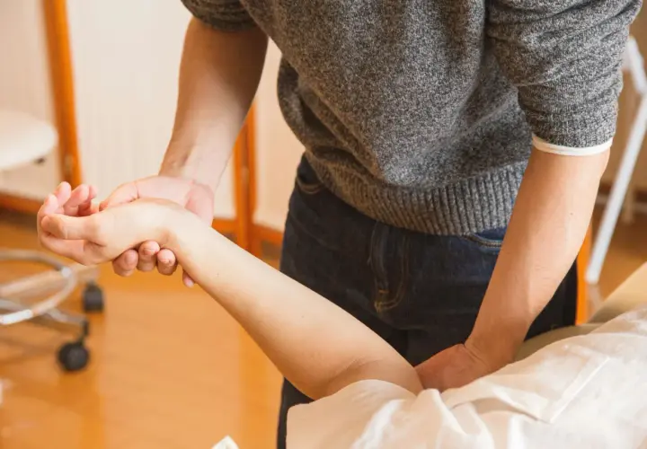 Fizjoterapeuta delikatnie masuje krzywą rękę po zdjęciu gipsu, pomagając przywrócić jej pełną sprawność.
