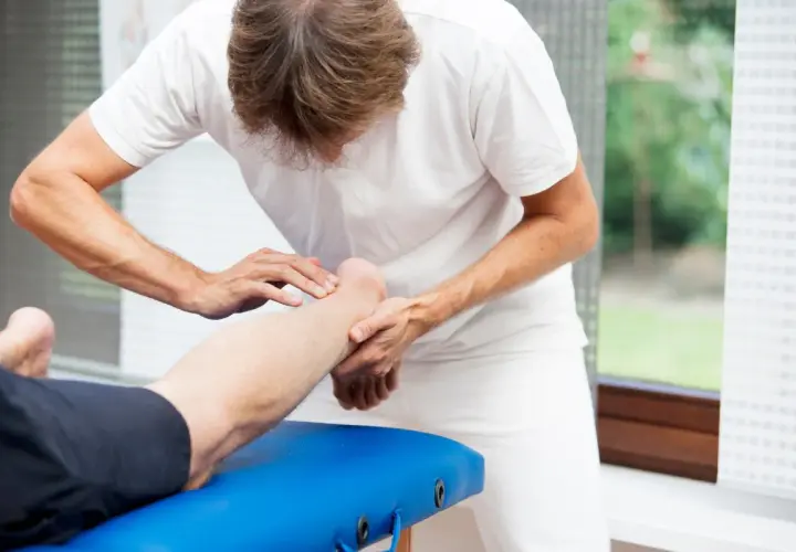 Fizjoterapeuta delikatnie masuje łydkę pacjenta, wspierając rehabilitację po zerwaniu ścięgna Achillesa.
