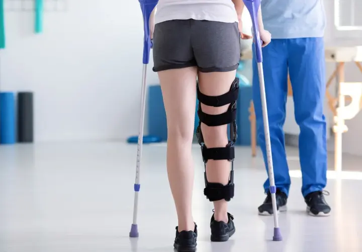 Rehabilitacja po zespoleniu gwoździem gamma. Pacjentka w ortezie na nodze, wspierając się kulami, rozpoczyna powrót do sprawności.