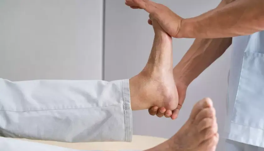 Fizjoterapeuta wykonuje ćwiczenia na opadającą stopę, delikatnie unosząc ją.