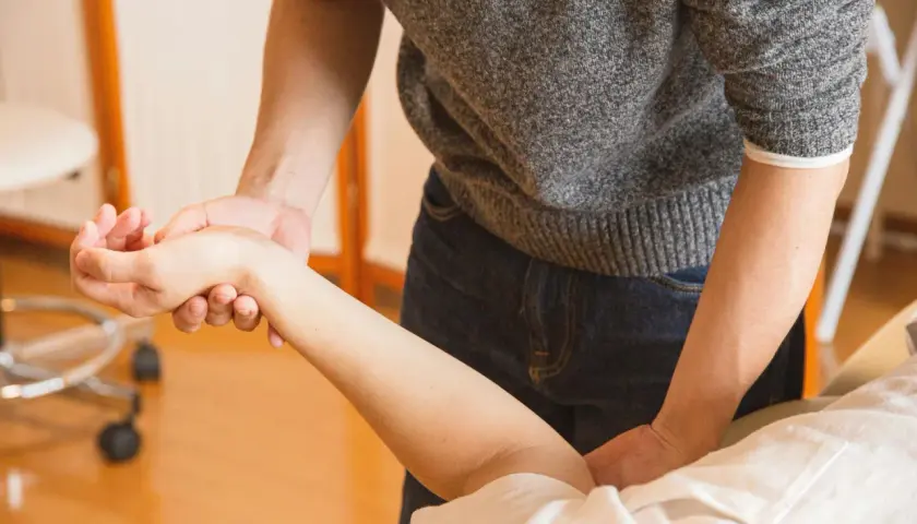 Fizjoterapeuta delikatnie masuje krzywą rękę po zdjęciu gipsu, pomagając przywrócić jej pełną sprawność.