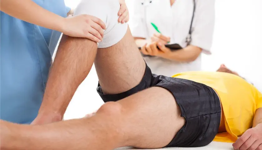 Fizjoterapeuta pomaga pacjentowi w rehabilitacji po zerwaniu więzadła krzyżowego przedniego (ACL).