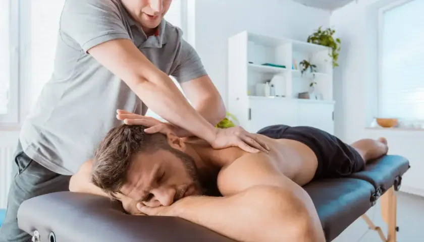 Fizjoterapeuta wykonuje masaż sportowy na plecach mężczyzny leżącego na kozetce.