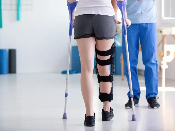 Rehabilitacja po zespoleniu gwoździem gamma. Pacjentka w ortezie na nodze, wspierając się kulami, rozpoczyna powrót do sprawności.